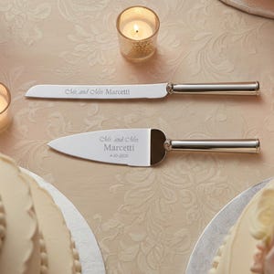 K&ouml;nnte beinhalten: Ein silberfarbenes Tortenmesser- und Tortenheber-Set mit polierten Metallgriffen. Die Messerklinge ist mit "Mr. and Mrs. Marcetti" graviert und der Tortenheber tr&auml;gt den Text "Mr. and Mrs. Marcetti" sowie das Datum "4-10-2026" in Schreibschrift.
