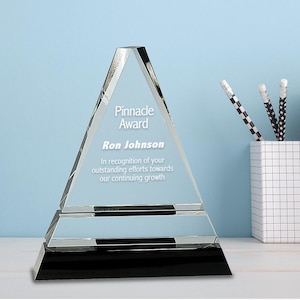 May include: A clear glass pyramid award with a black base. The award reads "Pinnacle Award" and "Ron Johnson" with the text "In recognition of your outstanding efforts towards our continuing growth".