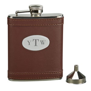 May include: A brown leather-covered flask with a silver top and a silver oval plaque with the initials "YTW" engraved on it. The flask comes with a silver funnel.