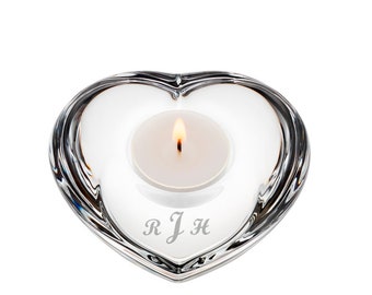 May include: A clear glass heart-shaped candle holder with a small white tea light candle burning inside. The holder has the initials "R J H" etched on the bottom.