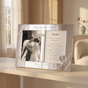 May include: A silver-toned double photo frame featuring the engraved text Happily Ever After at the top and Brian & Ashley October 10, 2027 at the bottom. The frame holds a black and white wedding photograph and a printed wedding invitation.