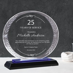 May include: A clear glass award with a blue base, featuring a laurel wreath design and the text "25 Years of Service". The award is presented to Michelle Anderson and includes the date December 2024.