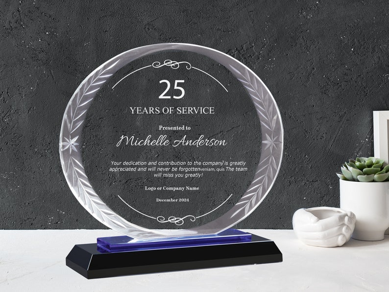 May include: A clear glass award with a blue base, featuring a laurel wreath design and the text "25 Years of Service". The award is presented to Michelle Anderson and includes the date December 2024.