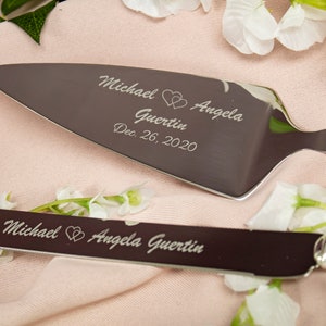 May include: A silver cake cutting set with two knives. The larger knife has the inscription "Michael Angela Guertin Dec. 26, 2020" with two hearts. The smaller knife has the inscription "Michael Angela Guertin" with two hearts.