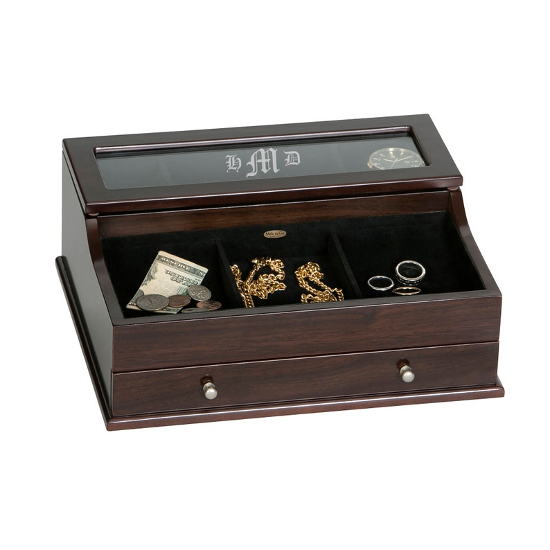 May include: A dark wood jewelry box with a glass top and a drawer. The top has the initials "LMD" etched into the glass. Inside are compartments with jewelry, money, and a watch.