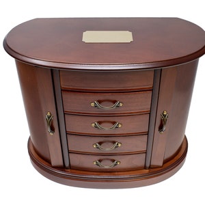 May include: A dark brown wooden jewelry box with a semi-circular top and a blank rectangular metal plate centered on the lid. The unit features four horizontal drawers and two side doors, all equipped with curved, antique-style metal handles.