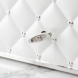 May include: Close-up of a white, quilted jewelry box with silver heart-shaped studs. The box features a silver handle with a textured design. The box has a silver trim and a white interior.