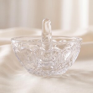 May include: A clear glass ring holder dish featuring a central vertical post for rings. The exterior of the bowl has a textured, repeating heart-shaped pattern. Etched into the glass are the letters B & A and the date 9.12.26.