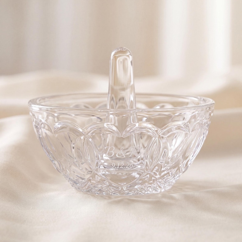 May include: A clear glass ring holder dish featuring a central vertical post for rings. The exterior of the bowl has a textured, repeating heart-shaped pattern. Etched into the glass are the letters B & A and the date 9.12.26.