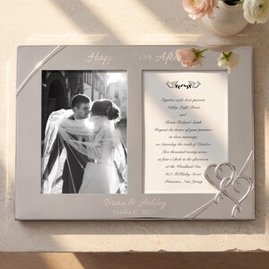 May include: A rectangular silver-toned metal double photo frame featuring the engraved text Happily Ever After at the top and Brian & Ashley October 10, 2027 at the bottom. The frame includes two heart-shaped metal accents and a wedding invitation.