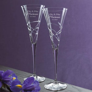 May include: Two clear glass champagne flutes with a swirling design. The flutes are engraved with the text "Mr. & Mrs. Mariani" and the date "11-2-2022".
