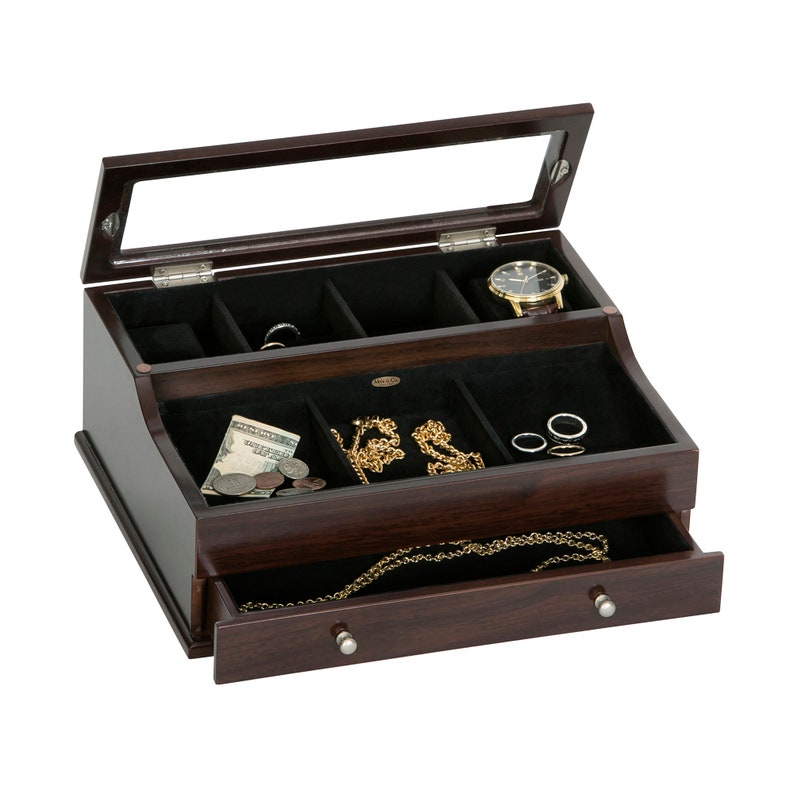 May include: A dark brown wooden jewelry box with a glass top, open to reveal compartments lined with black fabric. The box contains a watch, rings, necklaces, and money. A drawer is partially open, displaying a necklace. The box has silver knobs.