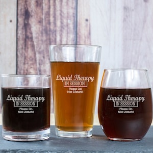 May include: Three glass tumblers with the text "Liquid Therapy In Session Please Do Not Disturb!" etched on them. The tumblers are filled with a dark liquid.