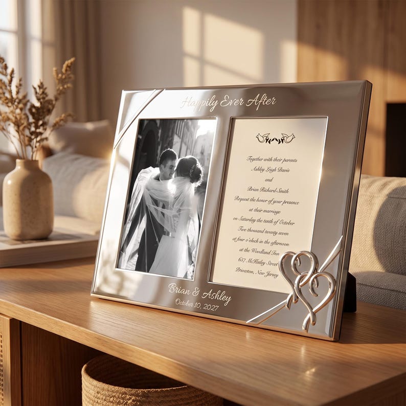May include: A silver-toned rectangular double photo frame featuring the engraved text Happily Ever After at the top and Brian & Ashley October 10, 2027 at the bottom. The frame includes a black and white wedding photo and a printed invitation.