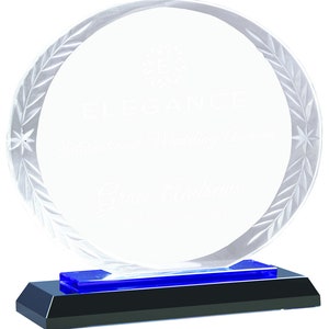 May include: A clear glass award with a blue base. The award has a circular design with a laurel wreath etched around the edge. The text "Elegance" is engraved on the award.
