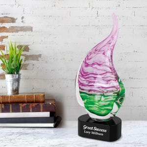 May include: A pink and green glass sculpture award with a black base. The base has the text "Great Success" and "Lory Milburn" engraved on it.