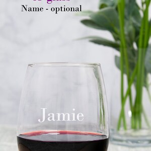 May include: A clear glass wine glass with the name "Jamie" etched on the side. The glass is filled with red wine.