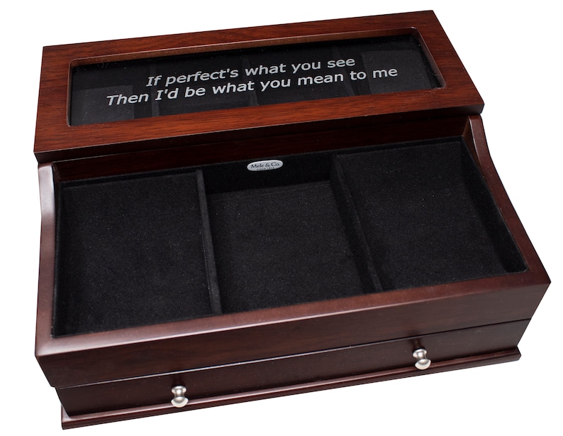 May include: A wooden jewelry box with a dark cherry finish. The box has a glass top with the inscription "If perfect's what you see Then I'd be what you mean to me." The interior is lined with black velvet and has multiple compartments and a drawer.