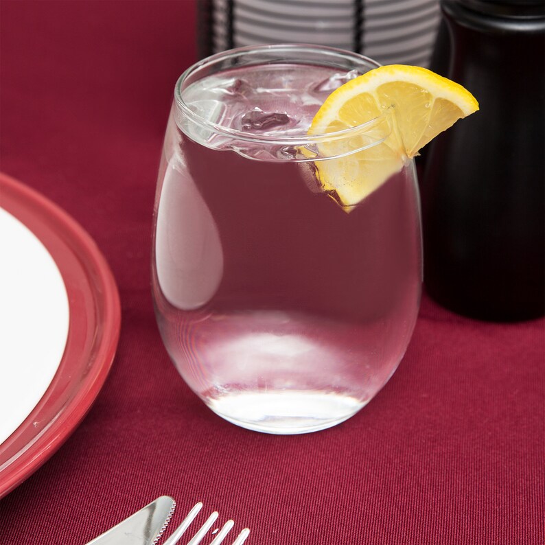 May include: A clear glass filled with water and ice with a lemon wedge on the rim. The glass is sitting on a red tablecloth.
