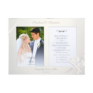 May include: A silver picture frame with two openings for photos. The frame has a silver ribbon design and a heart-shaped design on the bottom right corner. The frame has the text "Micheal & Christina" at the top and "Happily Ever After 6.24.2022" at the bottom. The frame is designed for a wedding.