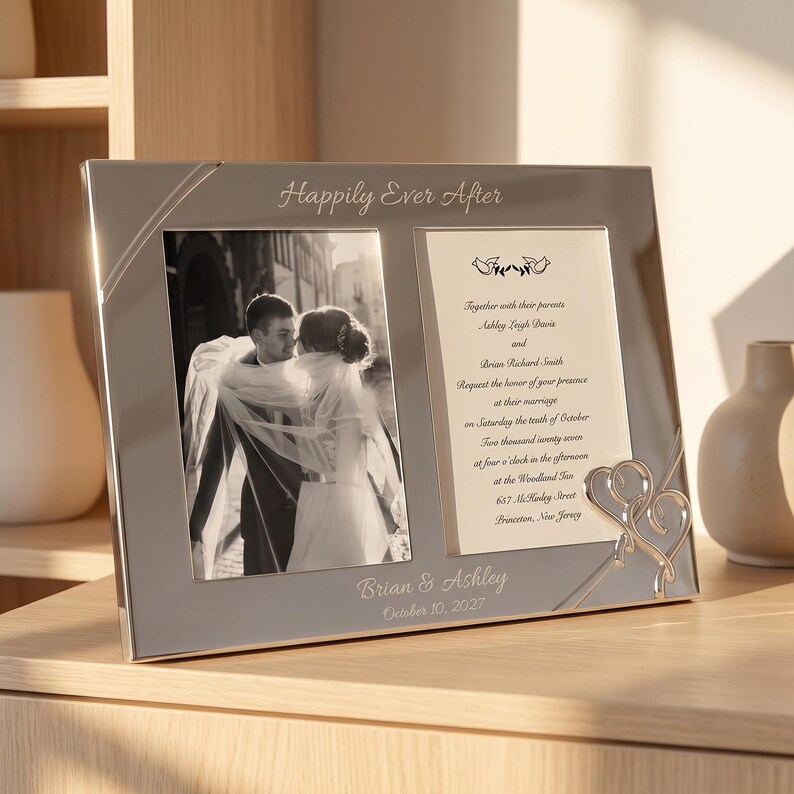 May include: A silver-toned double photo frame featuring the text "Happily Ever After" at the top and "Brian & Ashley October 10, 2027" at the bottom. The left side holds a black and white photo of a couple, while the right side displays wedding invitation text with two small bird icons and a decorative silver heart accent.