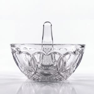 May include: A clear glass ring holder dish featuring a central vertical post and a scalloped rim. The exterior surface is etched with a diamond-cut pattern and includes the engraved text B&R and the date 9.17.26 on the front side.