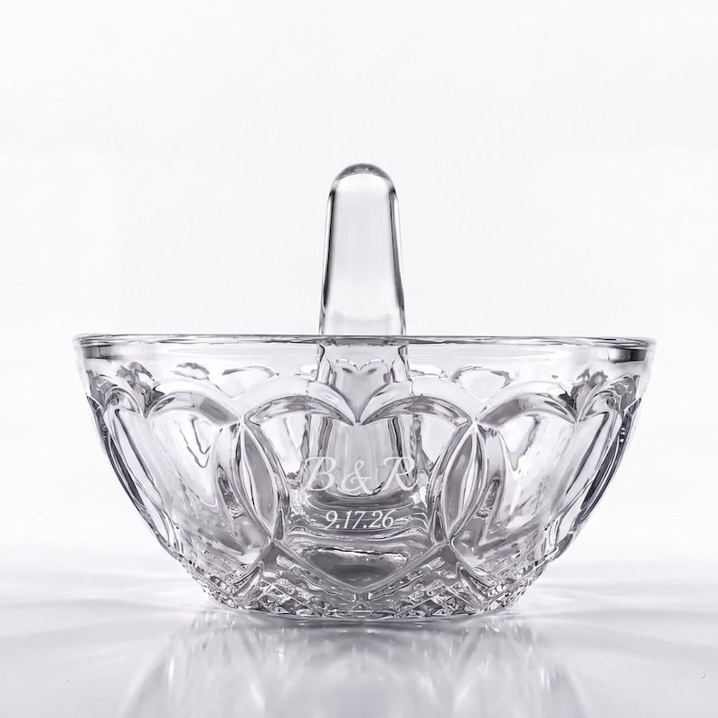 May include: A clear glass ring holder dish featuring a central vertical post and a scalloped rim. The exterior surface is etched with a diamond-cut pattern and includes the engraved text B&R and the date 9.17.26 on the front side.