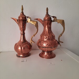 Peut inclure: Deux théières en cuivre avec des motifs ornés et des accents dorés. Les théières sont numérotées 1 et 2.