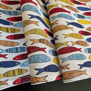 May include: Two fabric table runners with a repeating pattern of colorful fish. The fish are in shades of red, blue, yellow, and orange. The background is a light beige linen.