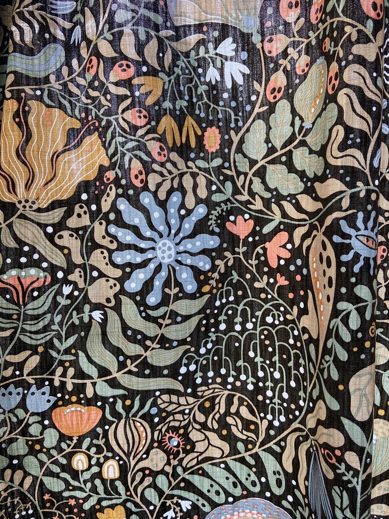 May include: A black fabric with a colorful floral pattern. The pattern features flowers, leaves, and other botanical elements in shades of blue, green, pink, and brown.