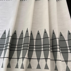 May include: White fabric curtains with a repeating pattern of gray fish. The fish are arranged in rows with horizontal lines, and a border of small fish decorates the top edge. The curtains are folded, showing the texture of the fabric.