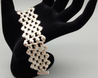 May include: A silver-toned bracelet with a geometric design, featuring a series of interconnected, star-shaped links. The bracelet is displayed on a black hand-shaped jewelry holder against a light gray background. The clasp is visible.