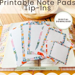 May include: Printable note pads with floral borders in blue, pink, and orange. The pads are displayed on an open book. The image includes the text "Printable Note Pads Tip-Ins" and "Digital Download".