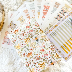 May include: A floral Bible cover with a bee and butterfly design, surrounded by coordinating Bible tabs. The cover features a white background with orange, yellow, and green floral elements. A list of Bible verses is also visible.