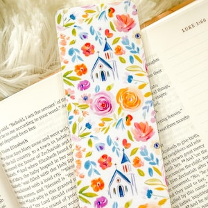 May include: A floral bookmark featuring watercolor illustrations of churches, roses, and other flowers in shades of pink, orange, blue, and green. The bookmark is placed in an open book with the text "LUKE 1:66".