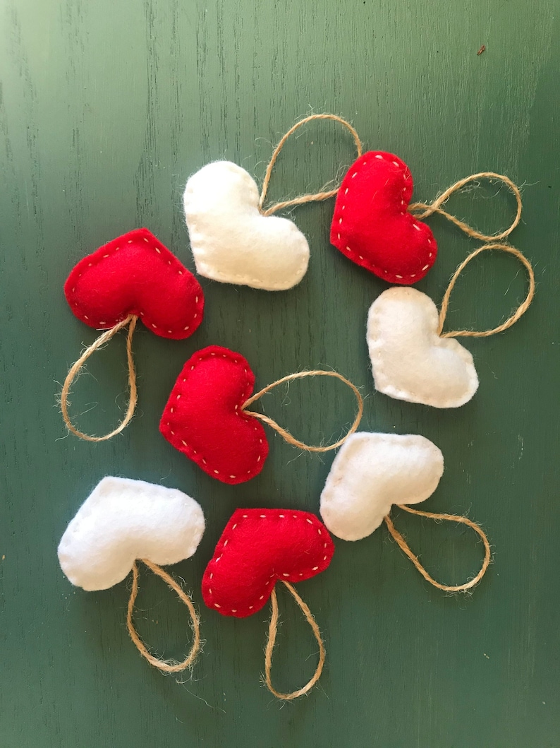 May include: A collection of eight heart-shaped ornaments crafted from felt in alternating red and white colors. Each heart features visible white stitching along the edges and includes a looped piece of natural jute twine for hanging purposes.