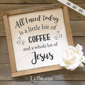 May include: A wooden framed sign with the text "All I need today is a little bit of COFFEE and a whole lot of Jesus" in black script. A white rose is in the bottom right corner. The sign is on a wooden surface.