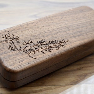 Könnte beinhalten: Eine Holzkiste mit einem eingravierten Blumenmuster auf der Oberseite. Die Kiste ist aus dunklem Holz und hat eine rechteckige Form.