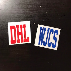 May include: Two white squares with red and blue lettering. The first square says "DHL" in red letters. The second square says "WJCS" in blue letters.