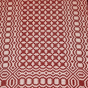 Op de afbeelding: Een geweven textiel met een herhalend geometrisch patroon in rood en gebroken wit. Het ontwerp bevat ruit- en ovale vormen, waardoor een textuur ontstaat. De stof wordt waarschijnlijk gebruikt voor woondecoratie of knutselen.