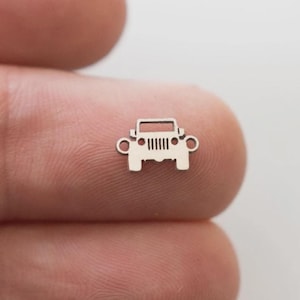 May include: A small, silver-colored charm in the shape of a Jeep. The charm has a detailed front grill, headlights, and a rectangular roof. The charm is held between two fingers against a blurred background.