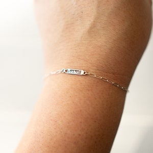May include: A silver chain bracelet with a small rectangular charm that says "MCMXCII".