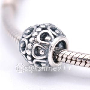 May include: A silver charm bead with an intricate openwork pattern of raised dots and teardrop shapes, threaded onto a silver snake chain bracelet. The bead features a dark oxidized finish in the recessed areas and the text @stylishme911.