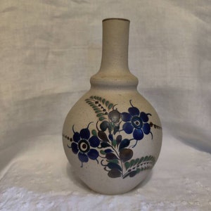 May include: A white ceramic vase with a narrow neck and a round body. The vase is decorated with blue, green, and brown floral designs.