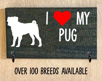 May include: A rectangular wooden sign with the words "I ❤️ MY PUG" in white lettering and a red heart. A white silhouette of a pug is on the left. Two black hooks are attached. The text "OVER 100 BREEDS AVAILABLE" is at the bottom.