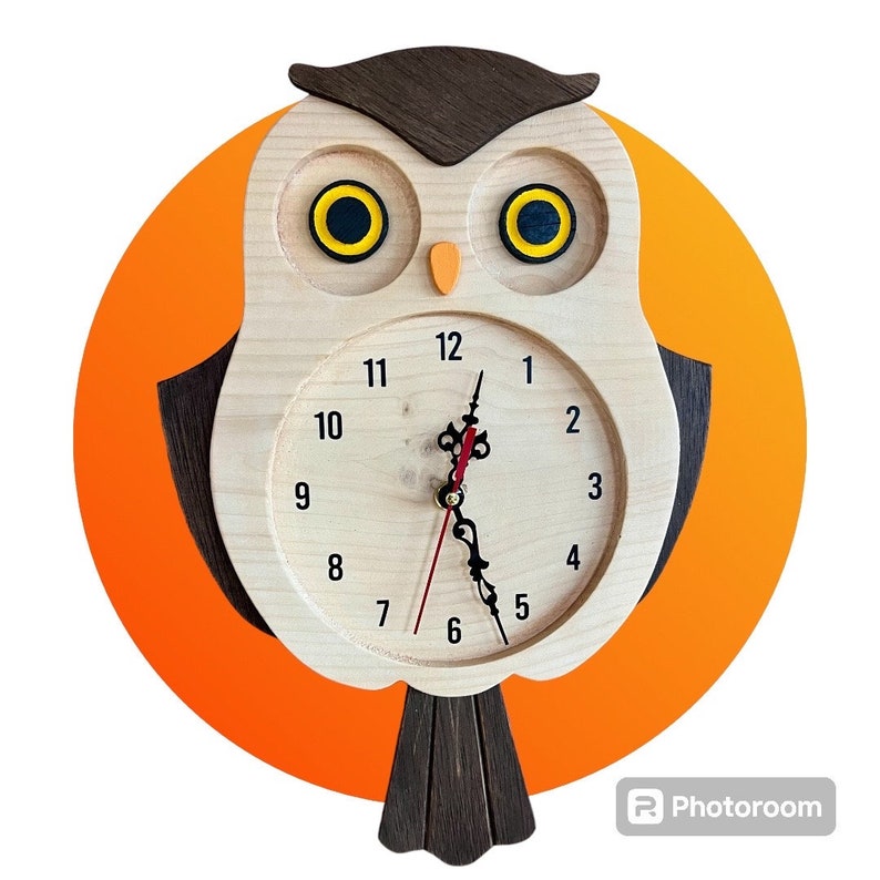 Puede incluir: Un reloj de madera con forma de b&uacute;ho con una cara marr&oacute;n y ojos amarillos. El reloj tiene un fondo blanco con n&uacute;meros y manecillas negros. El b&uacute;ho est&aacute; posado en una rama con un fondo naranja.