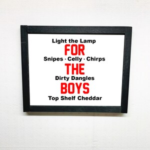 May include: A framed print with the text "Light the Lamp FOR Snipes. Celly. Chirps THE Dirty Dangles BOYS Top Shelf Cheddar" in red letters on a white background.