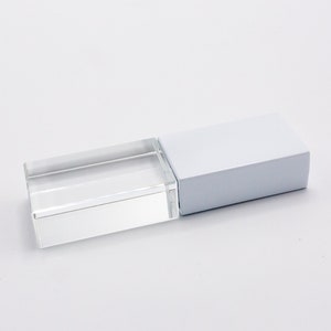 K&ouml;nnte beinhalten: Ein rechteckiger USB-Stick mit einem klaren, transparenten Acrylgeh&auml;use auf der einen Seite und einer festen, undurchsichtigen wei&szlig;en Kappe auf der anderen. Das Ger&auml;t hat ein schlankes, geometrisches Design mit scharfen Kanten und einer glatten Oberfl&auml;che.
