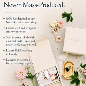 May include: A cream-coloured fabric-covered box with a lid, containing a photograph and a small gold object. The box features the text 'Not Generic. Never Mass-Produced.' and 'Anastasia Strates'. It is surrounded by pink and white flowers.