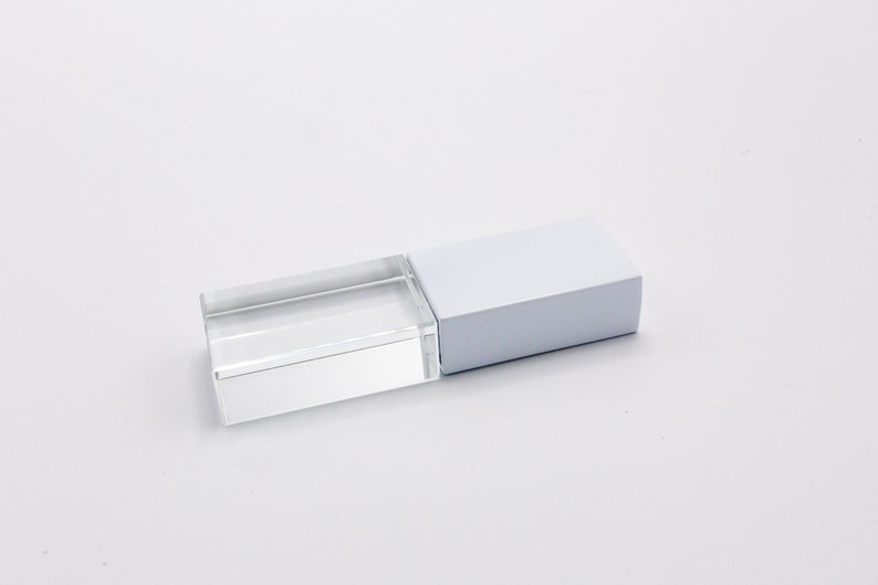 K&ouml;nnte beinhalten: Ein rechteckiger USB-Stick mit einem klaren, transparenten Acrylgeh&auml;use auf der einen Seite und einer festen, undurchsichtigen wei&szlig;en Kappe auf der anderen. Das Ger&auml;t hat ein schlankes, geometrisches Design mit scharfen Kanten und einer glatten Oberfl&auml;che.